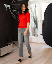 Woman wearing a coral red short sleeve cable knit sweater, walking in studio.