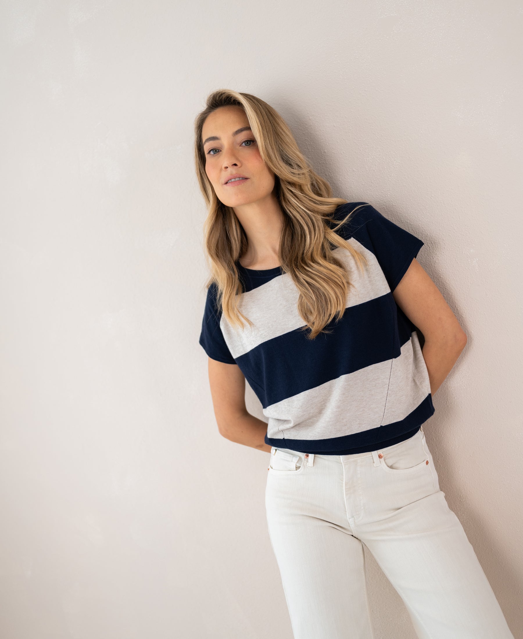 Woman wears a PLEIN PUBLIQUE striped sweater called THE LA PALOISE against a light wall.
