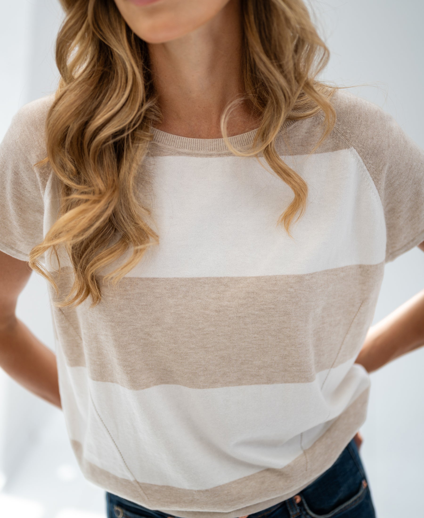 Woman wearing PLEIN PUBLIQUE striped sweater LA PALOISE in sand-ivory, hands behind back.