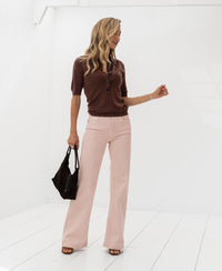 Woman wearing a Plein Publique merino wool polo shirt in brown, standing in a bright white room.