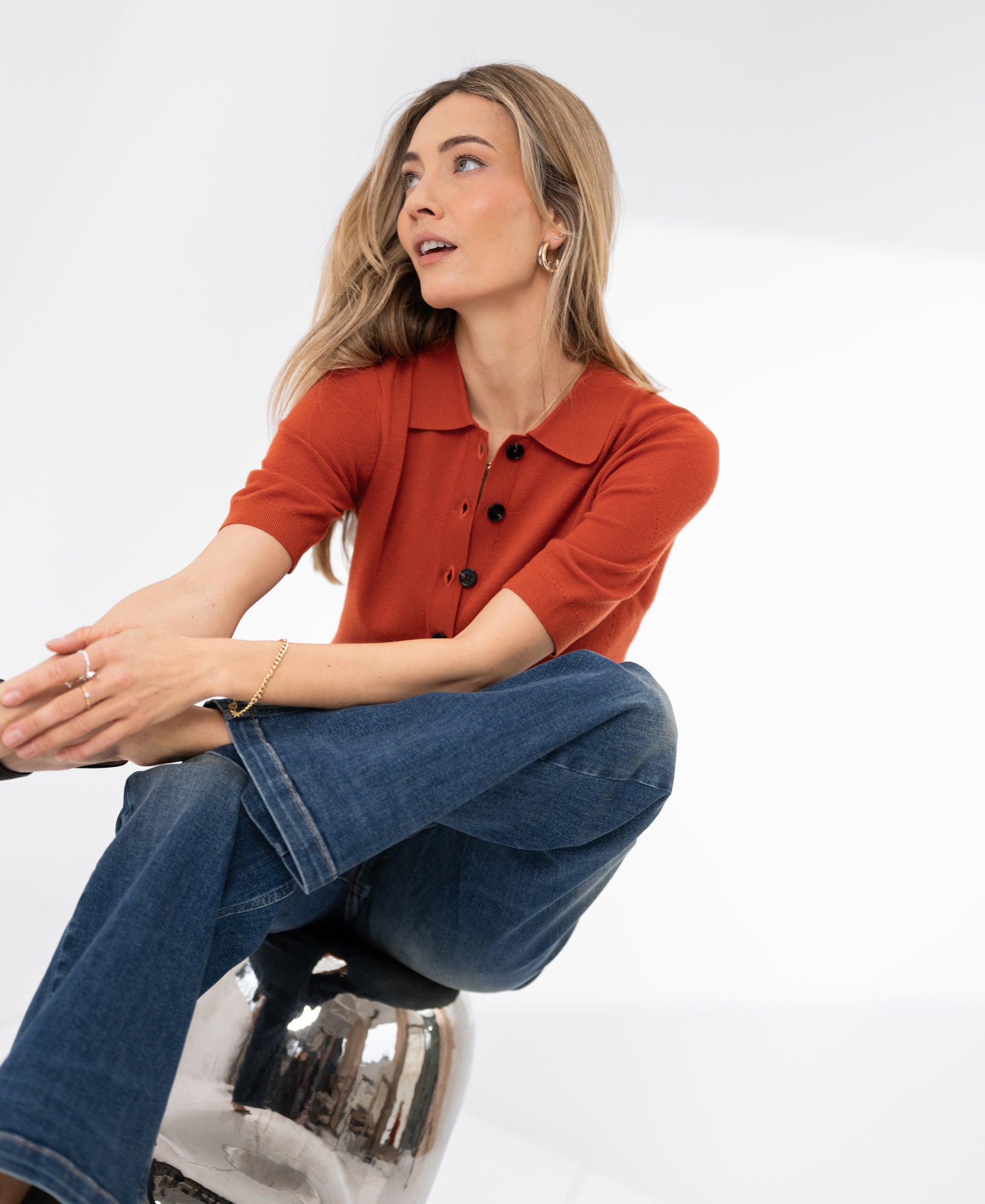 Woman wearing a merino wool polo shirt in cayenne, sitting and smiling.