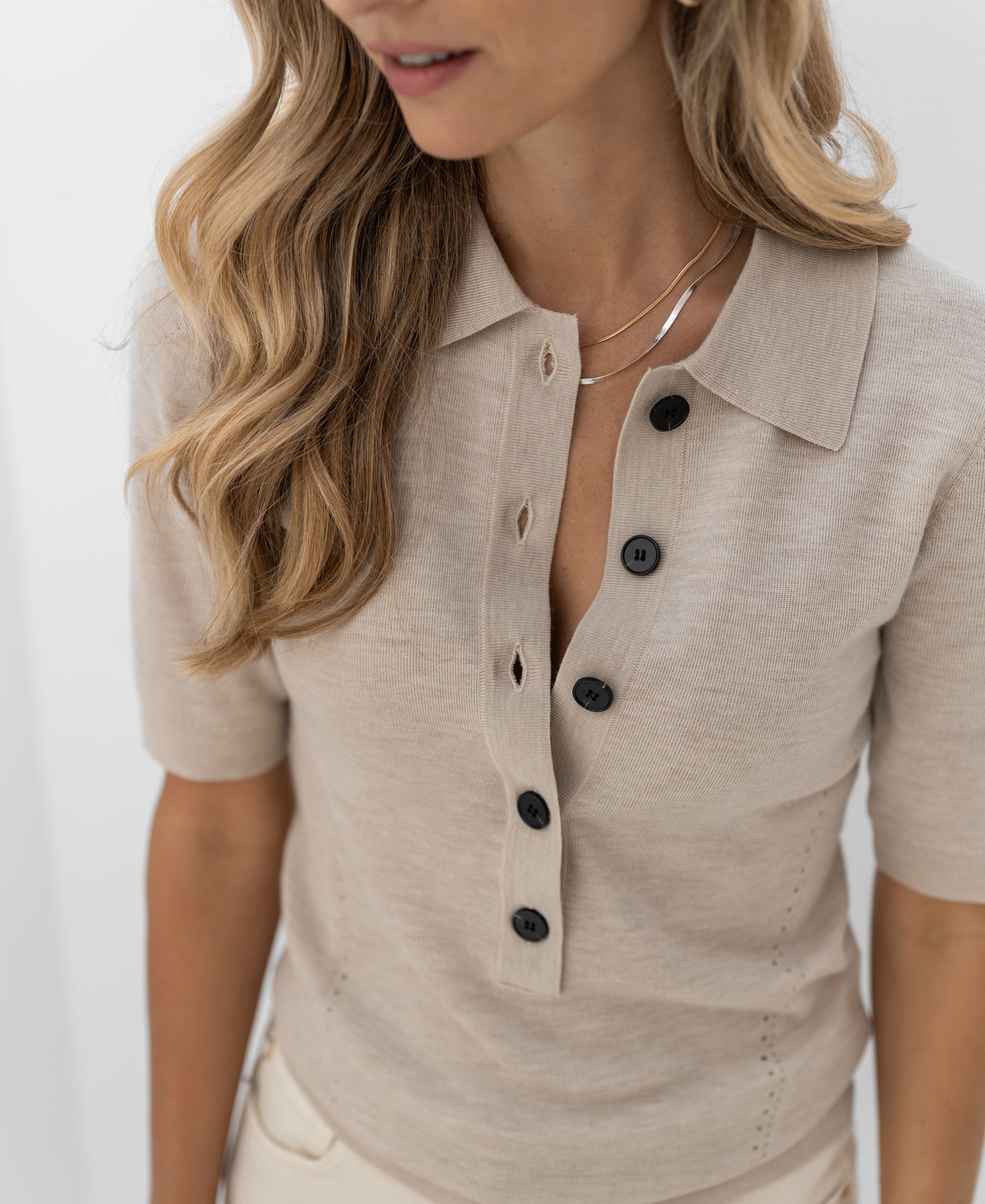 Beige merino wool polo shirt with black buttons, shoulders-up view.
