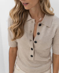 Beige merino wool polo shirt with black buttons, shoulders-up view.