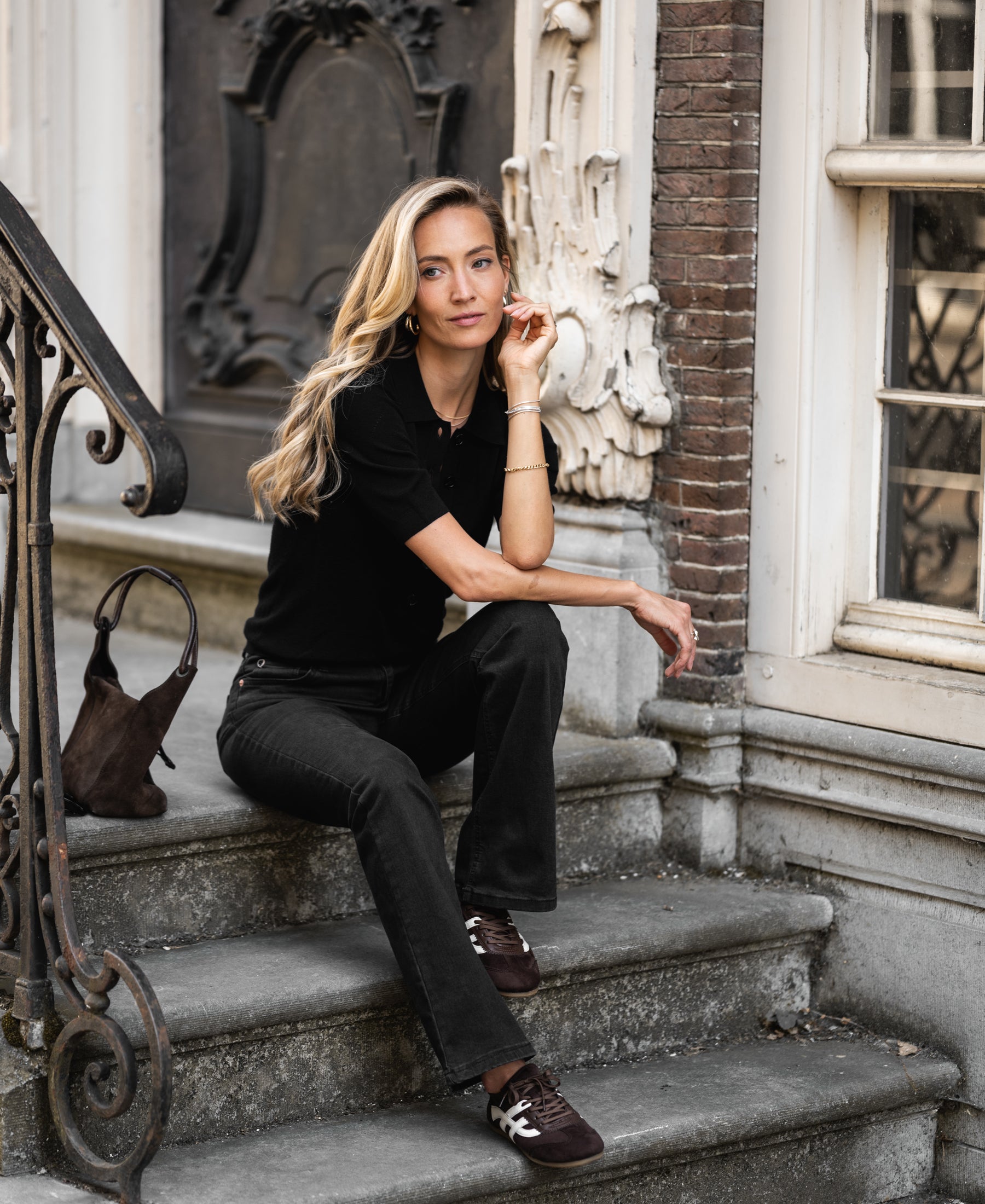 Black merino wool polo shirt by PLEIN PUBLIQUE LA PANTIN, shown worn by a woman sitting on steps.