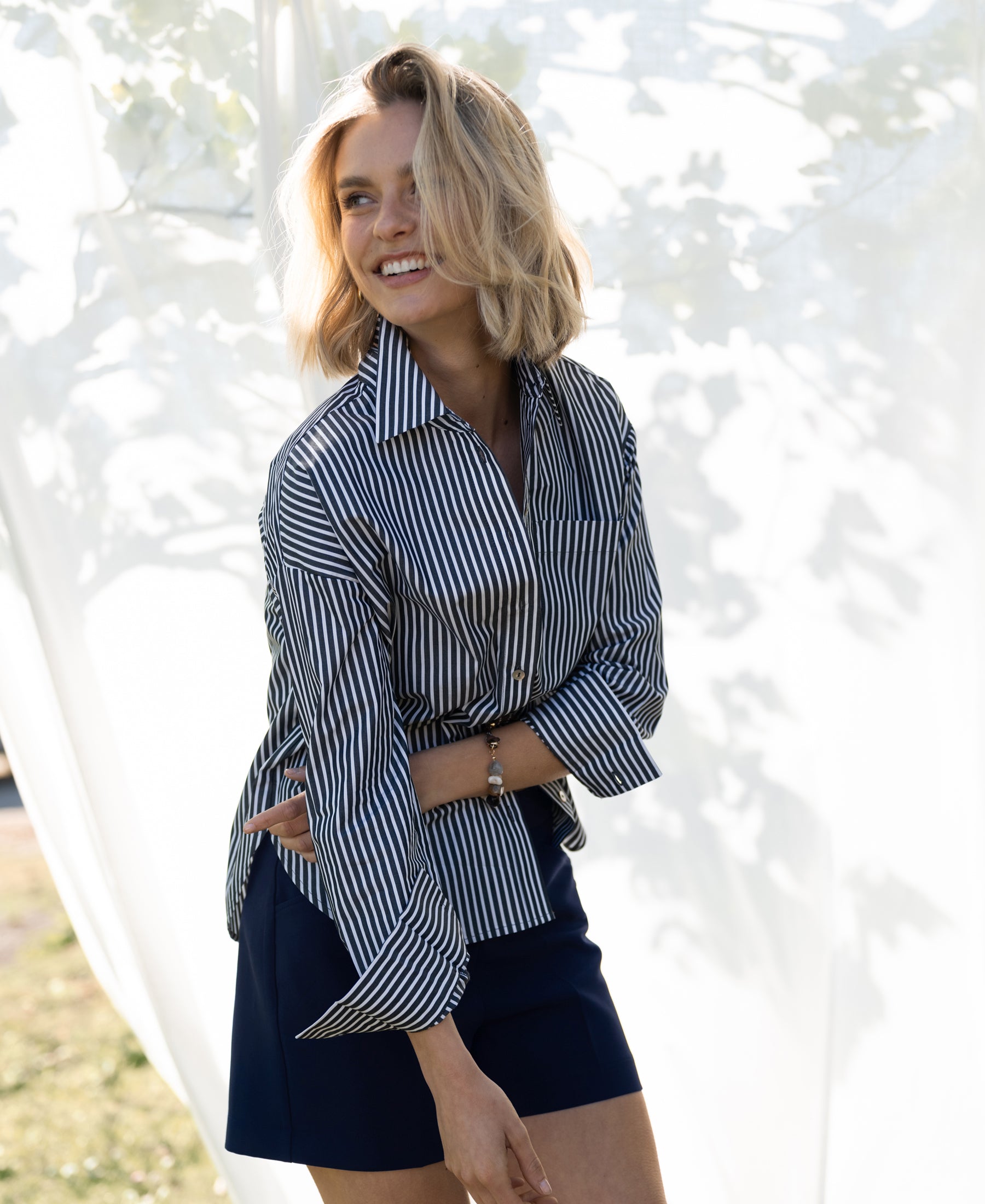 Striped white and anthracite Plein Publique LA PASCALLE blouse shown outdoors before a white backdrop.