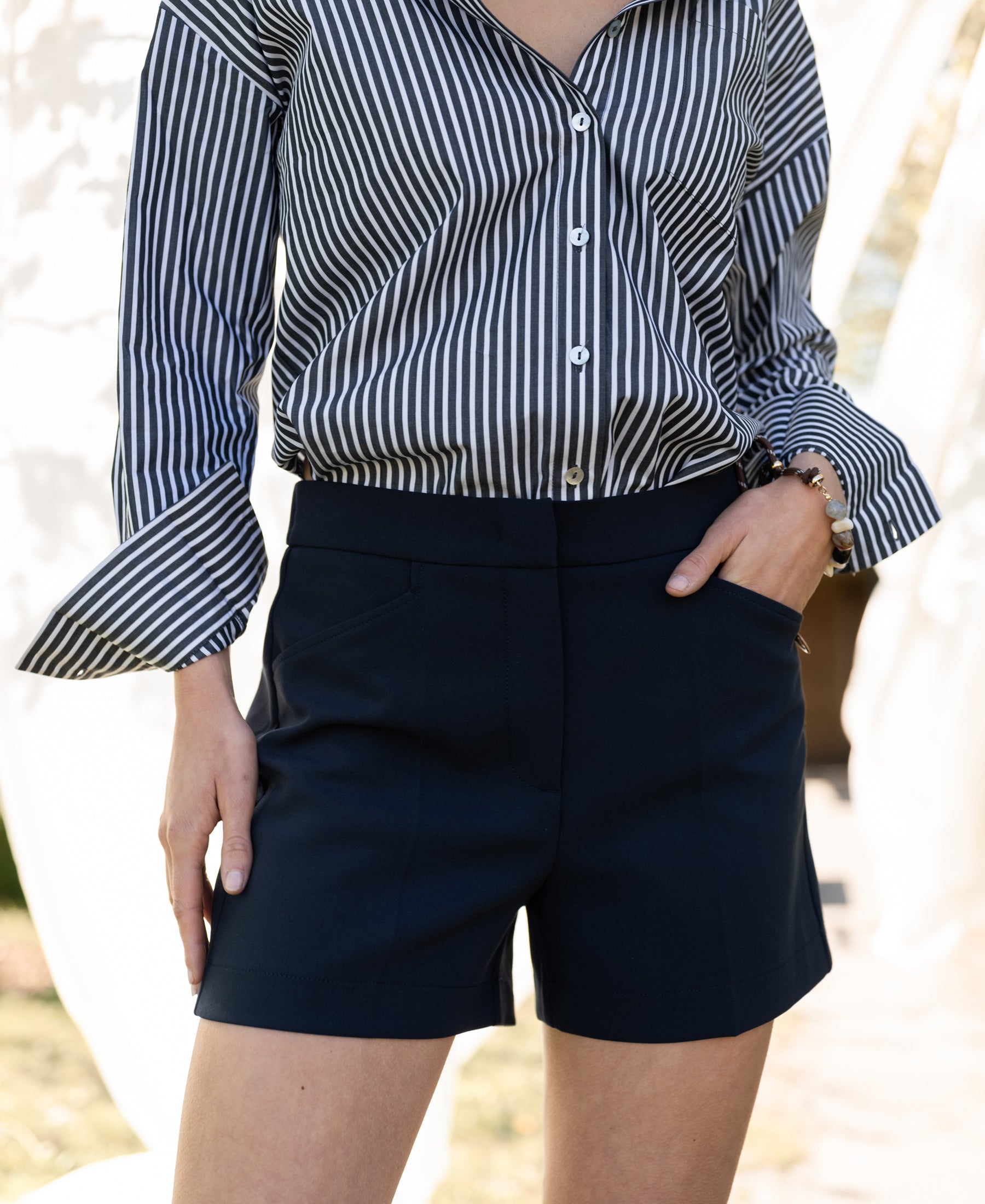 Navy blue LA MADDY shorts by PLEIN PUBLIQUE, shown outdoors with a hand in the pocket.