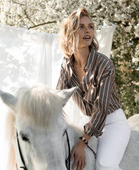 Brown-ivory striped Tencel blouse by Plein Publique, shown outdoors under blossoming trees.