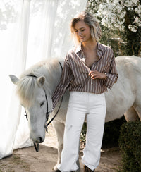 Woman wearing a Tencel blouse stands outdoors by a white horse and blossoming tree.