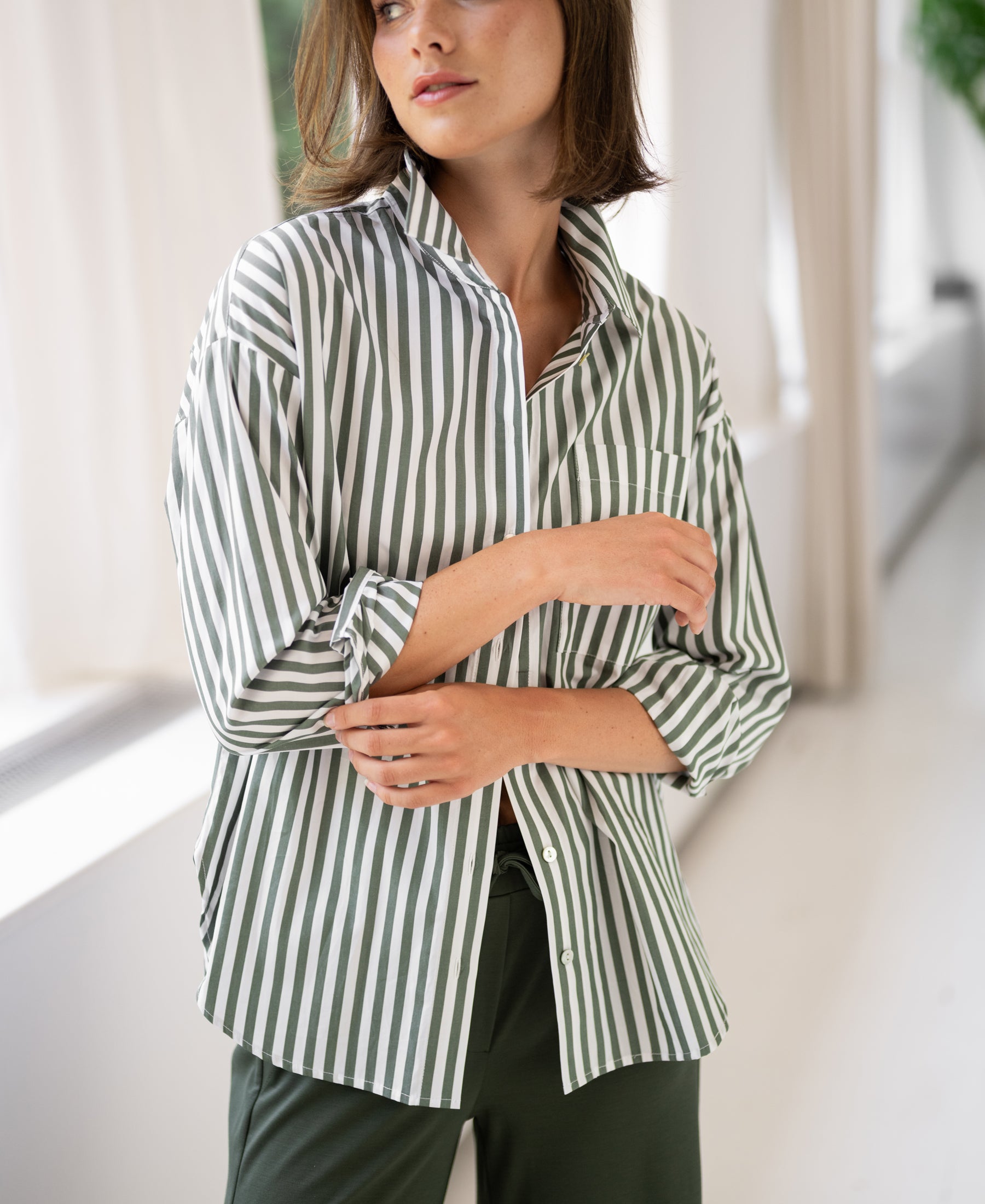 Oversized Plein Publique LA Pascale white-olive green striped blouse, worn by a woman standing by large windows.