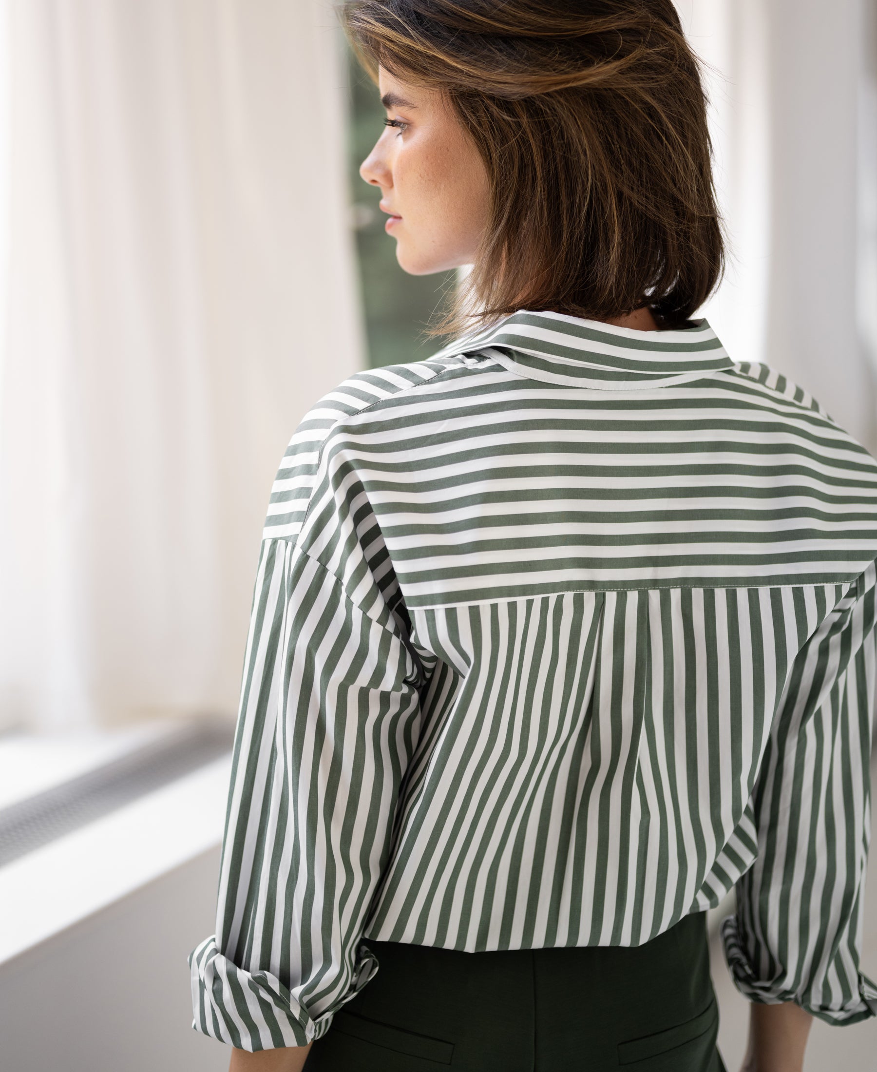 Back view of PLEIN PUBLIQUEs LA PASCALLE white-olive green striped blouse, shown indoors.