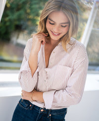 Woman wearing a PLEIN PUBLIQUE blouse, white and dark red striped, smiling and touching her collar.