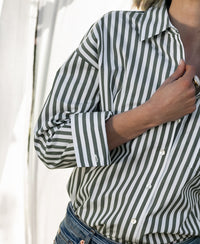 Woman wearing a white and olive green striped blouse, holding the collar.