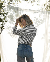 White and olive-green striped PLEIN PUBLIQUE LA PASCALLE blouse shown outside by a sheer white curtain.