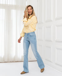 Woman wears light-wash flared jeans in a bright room with white curtains.