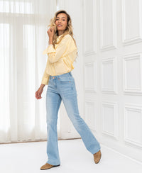 Woman wears OVERIG’s Les Flares bleached jeans, posing in a sunny room with large windows.