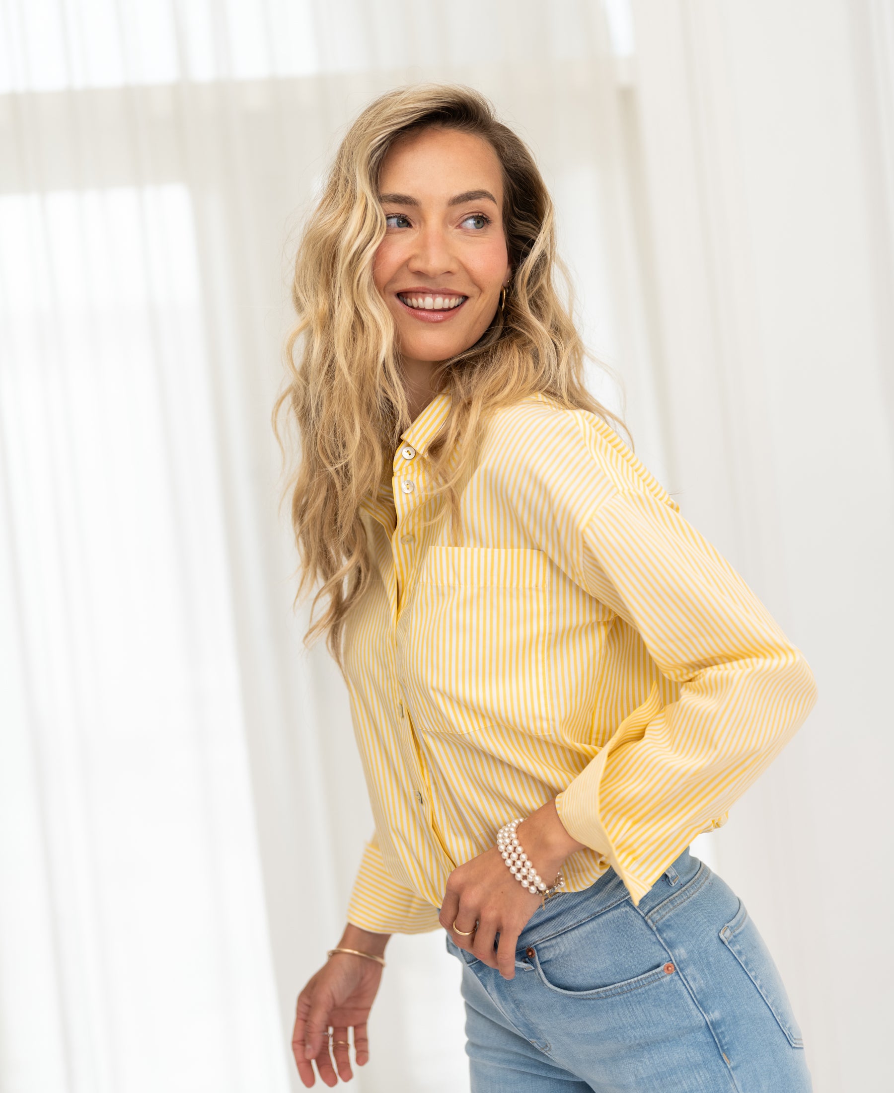 Yellow striped LA PASCALLE blouse by PLEIN PUBLIQUE shown worn in front of sheer white curtains.