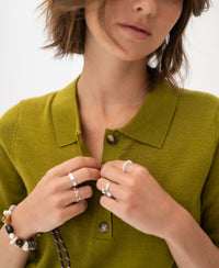 Woman wearing an olive green merino-silk polo shirt, adjusting a button.