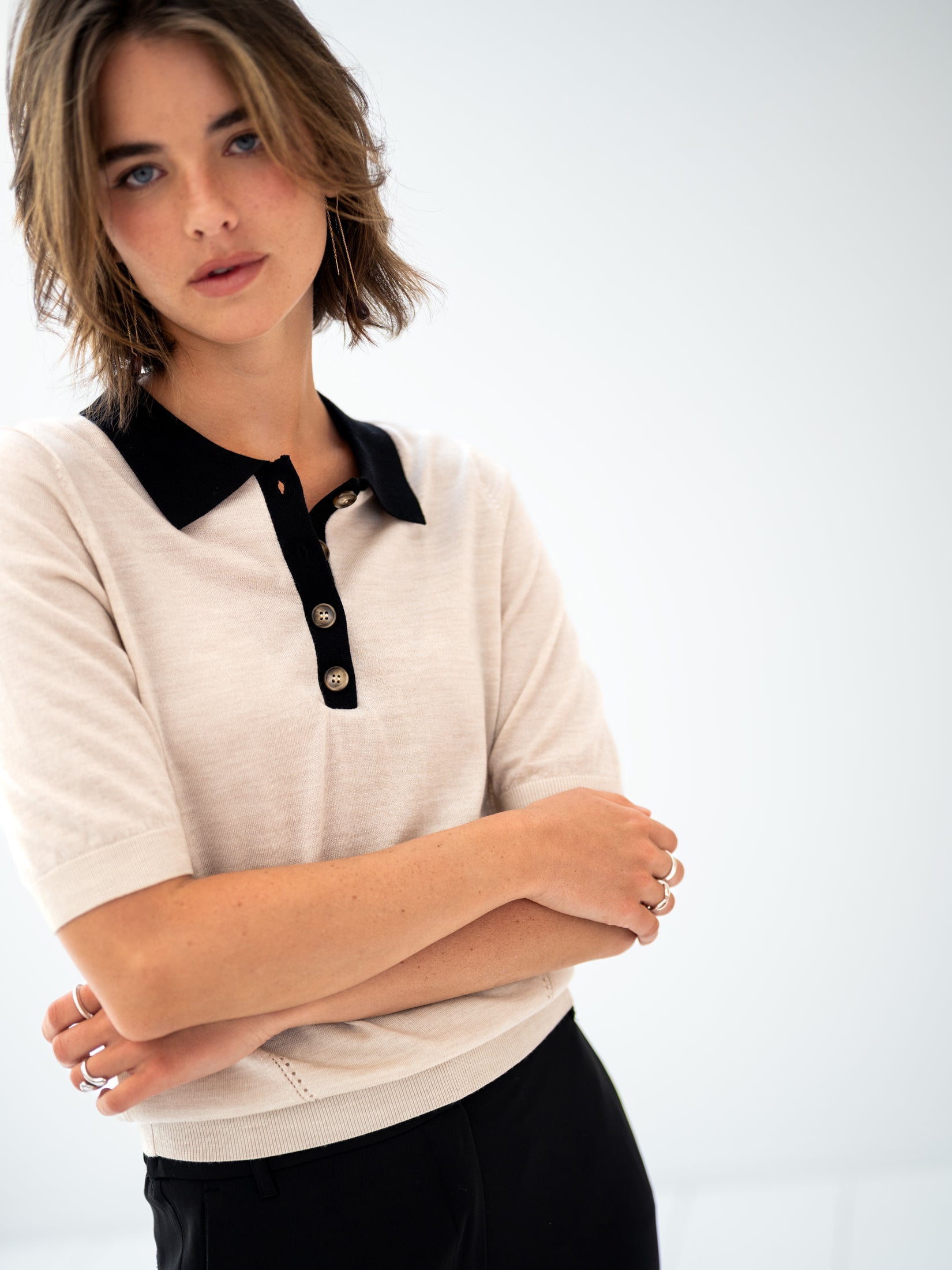 Merino wool-silk polo shirt in sand-black by PLEIN PUBLIQUE, shown with arms crossed.