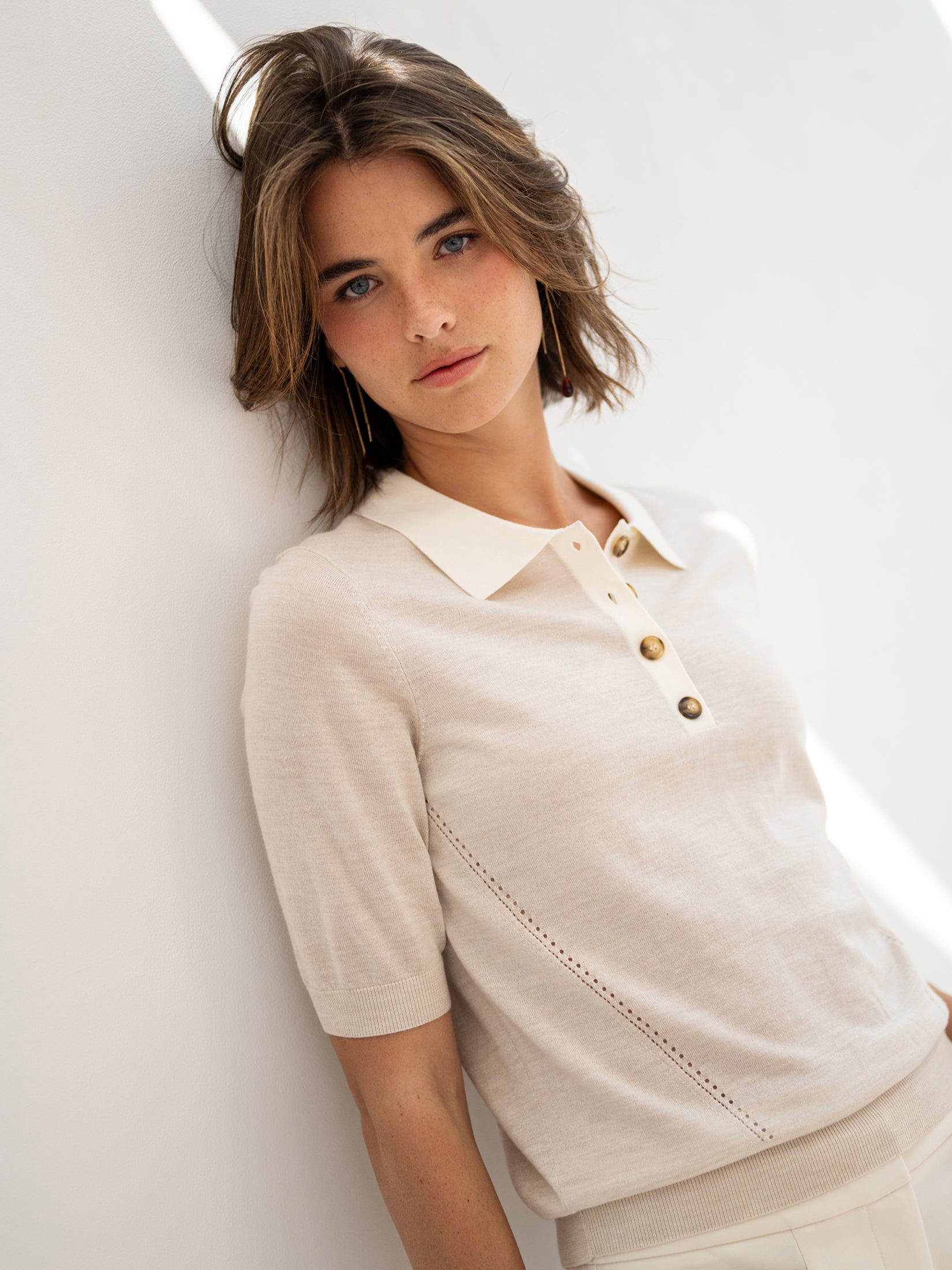 Merino silk polo shirt in sand and ivory, shown against a white wall.