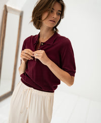 Woman wearing a Merino wool and silk polo shirt in wine color stands indoors with hands near her collar.