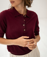 Merino wool-silk polo shirt in plum, shown on woman with hands clasped, light background.