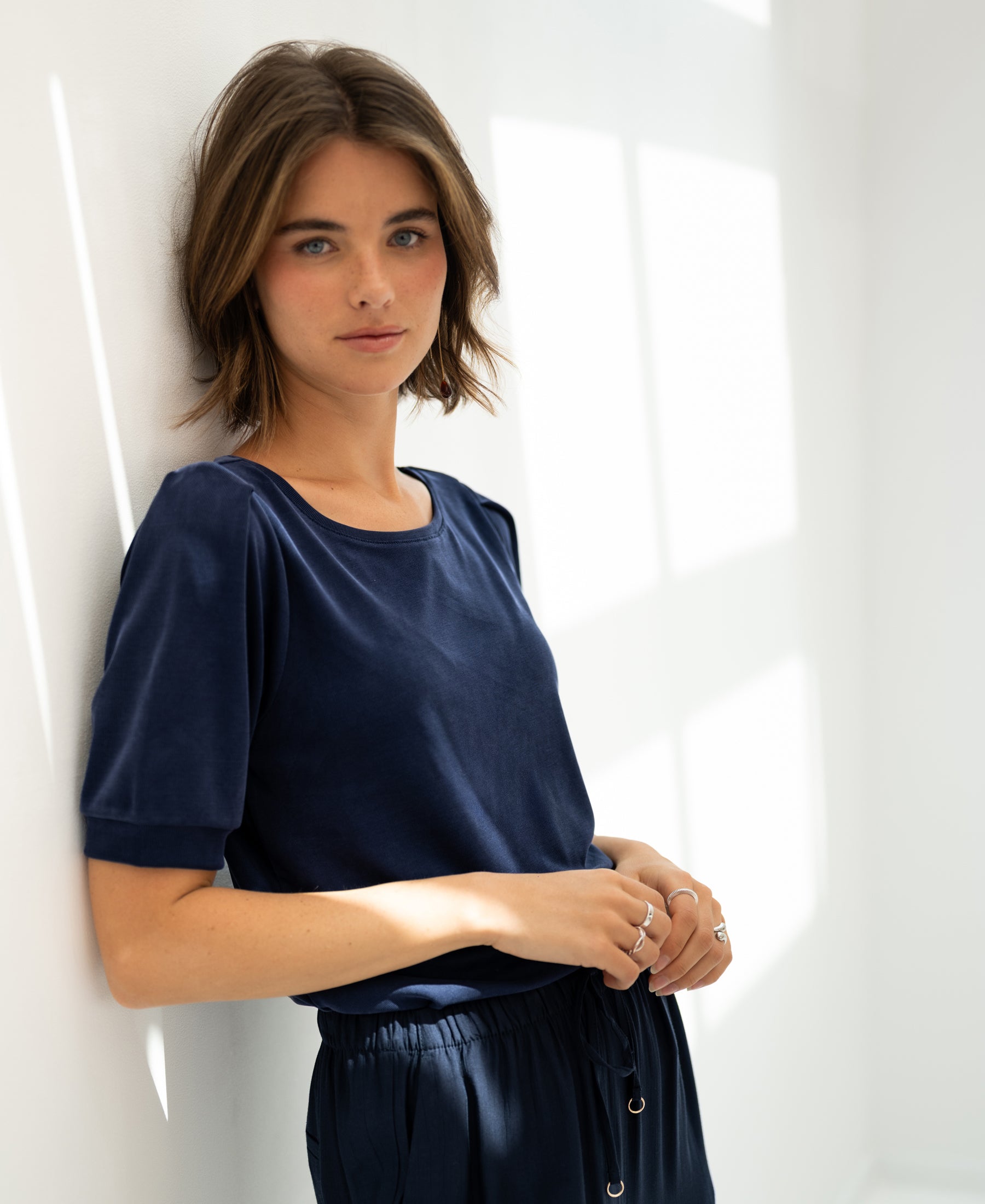 Woman wearing a dark blue ribbed T-shirt, sunlight streaming in.