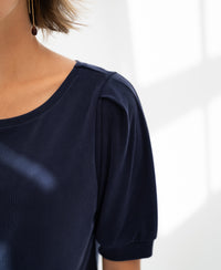 Close-up of a navy blue ribbed T-shirt with elegant pleated sleeves, shown by a window.
