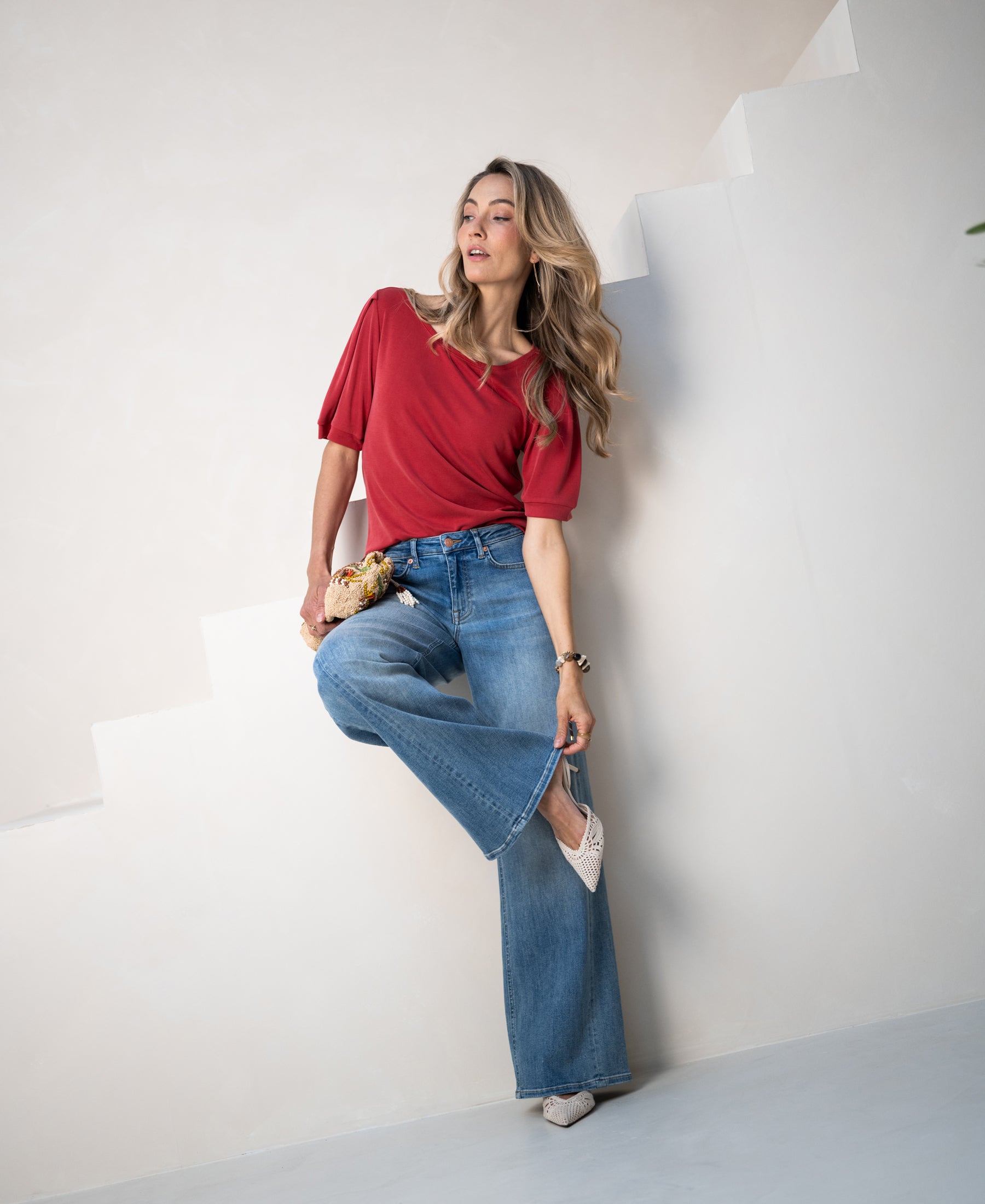 Woman wears wide leg jeans in light stone wash, standing on white stairs with a flower bouquet.