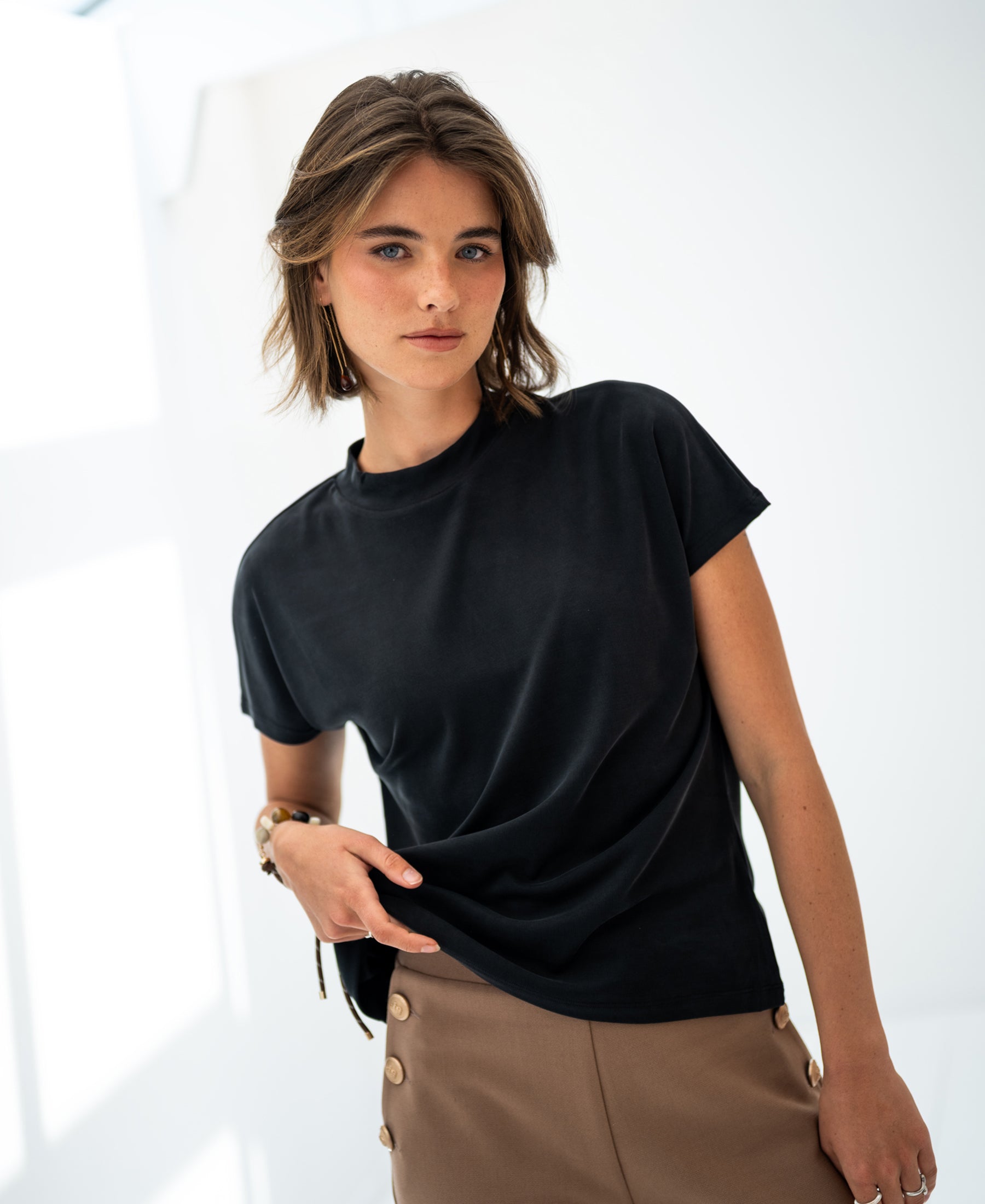 Woman with short brown hair wears the PLEIN PUBLIQUE ribbed collared top in charcoal, shown in soft natural light.