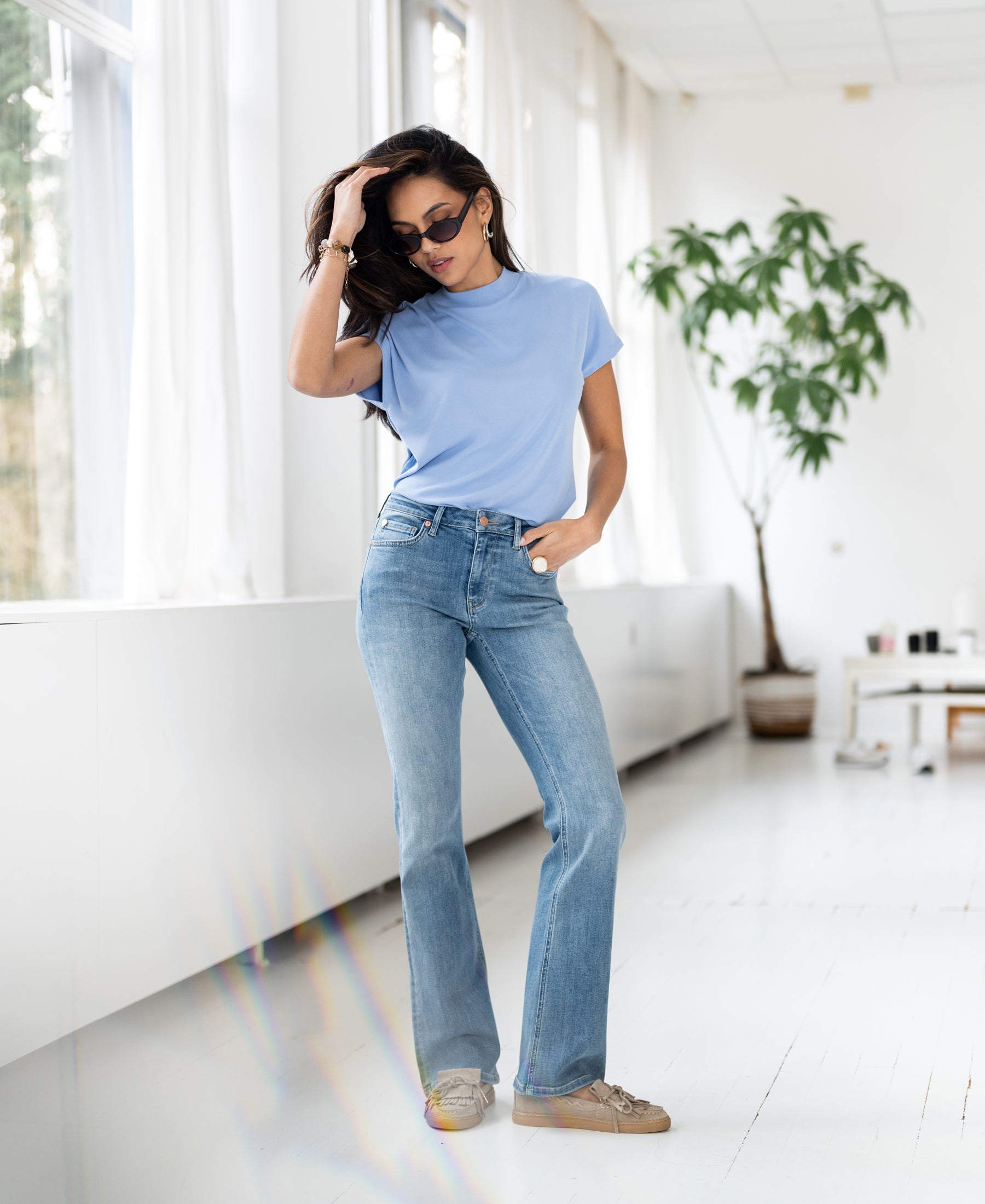Woman wears light blue ribbed collared top from PLEIN PUBLIQUE, photographed indoors.
