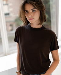 Woman wears brown ribbed top called LA PIERRE Choco by PLEIN PUBLIQUE, shown indoors near windows.