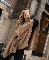 Camel and black merino wool poncho, shown on model against a city street background.