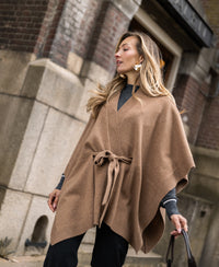 Woman wearing a camel-colored merino wool poncho walks outside.