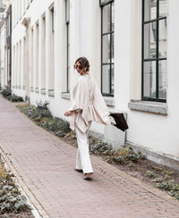 Light sand merino wool poncho by PLEIN PUBLIQUE, shown on model walking outside.