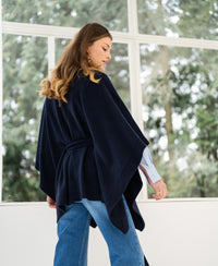 PLEIN PUBLIQUE dark blue merino wool poncho shown indoors by sunlit windows.