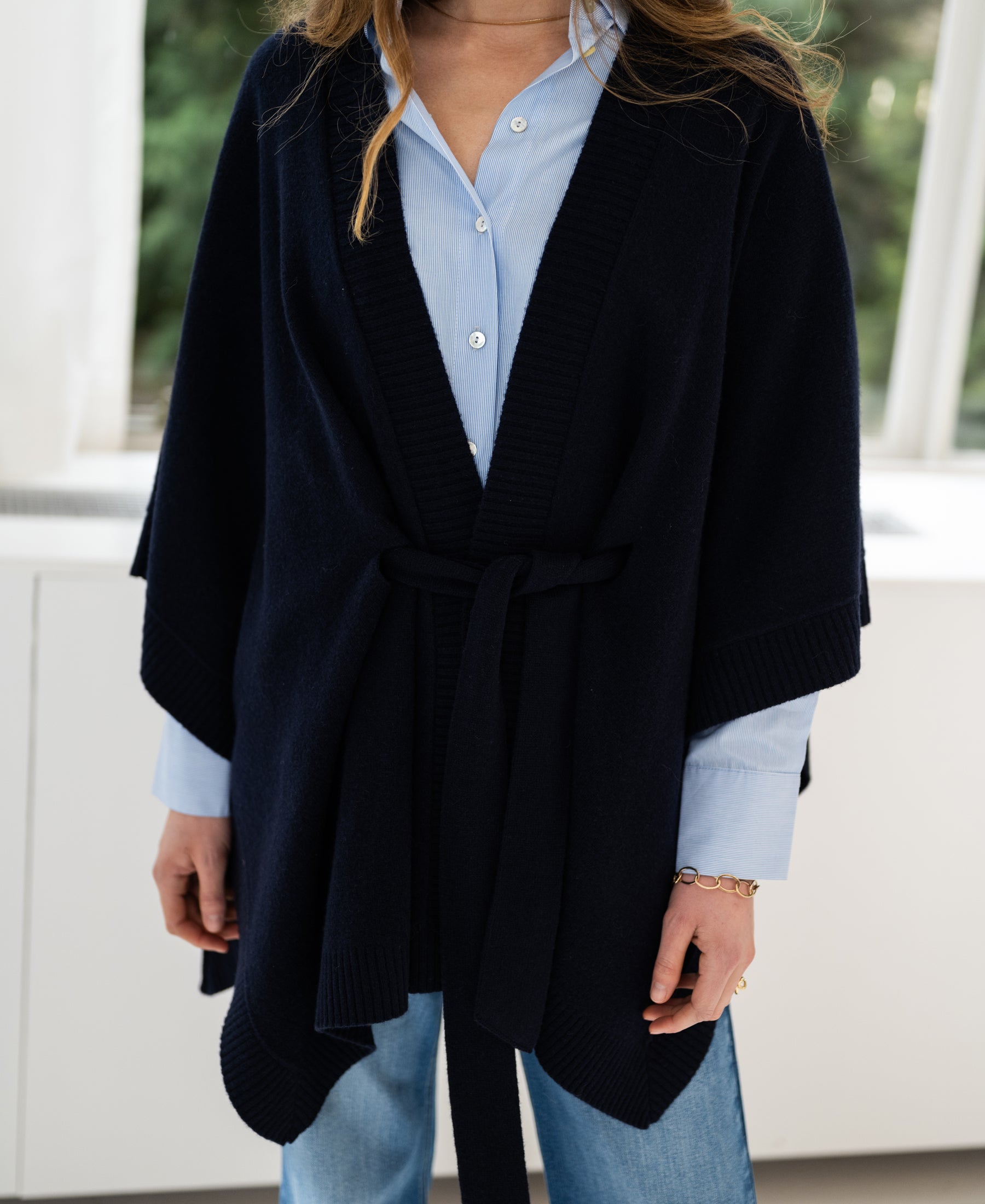 Dark blue merino wool poncho by PLEIN PUBLIQUE shown on a woman standing by a window.