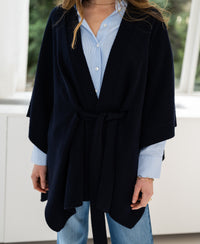 Dark blue merino wool poncho by PLEIN PUBLIQUE shown on a woman standing by a window.