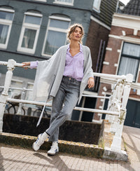 Merino wool poncho in silver grey by PLEIN PUBLIQUE, shown worn outdoors while leaning on a white railing.