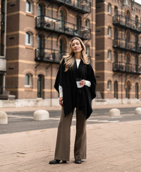 Black merino wool poncho by Plein Publique shown on a model standing outdoors.