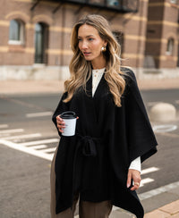 Black merino wool poncho by PLEIN PUBLIQUE shown outdoors.