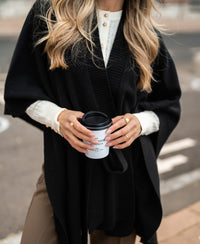 Black merino wool poncho by PLEIN PUBLIQUE shown on a woman outdoors.