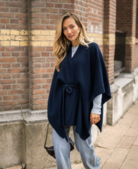 Dark blue merino wool poncho, shown from the front, worn by a woman walking outdoors.