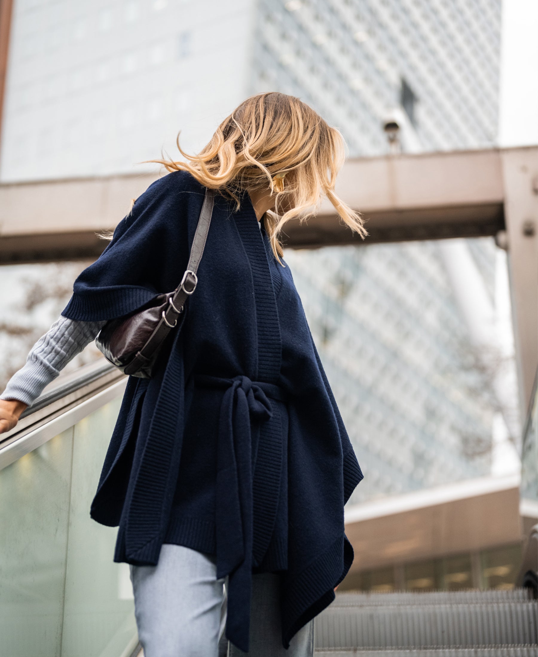 Navy blue merino wool poncho shown on model, city buildings in the background.