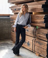 Black denim flared jeans by PLEIN PUBLIQUE, shown worn by a woman standing in a warehouse.