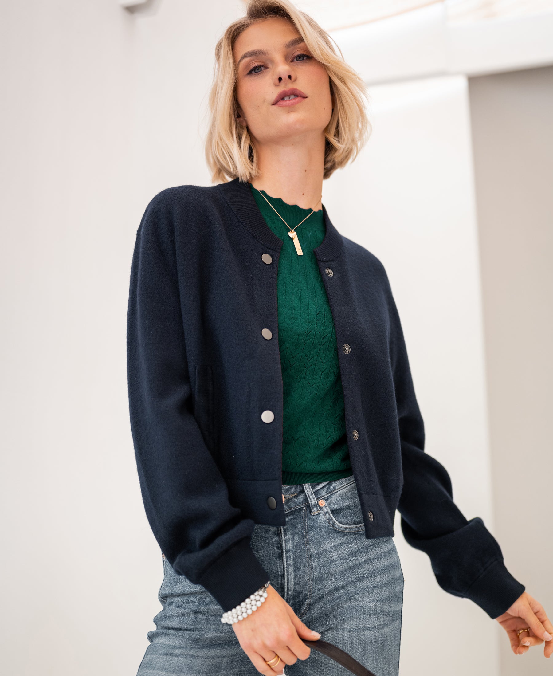 Woman wearing dark blue LA BOMBA bomber jacket against a light indoor background.