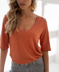 Woman wearing the PLEIN PUBLIQUE linen t-shirt in terra color, shown in soft natural light.