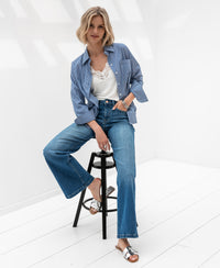 Woman wearing stonewash wide leg jeans sits on a black stool.