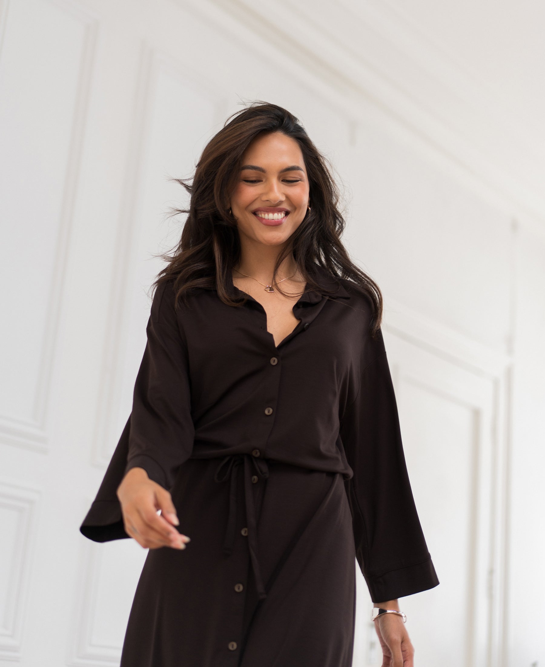 Front view of the PLEIN PUBLIQUE button-through dress in Pure Choco, shown indoors against a white wall.