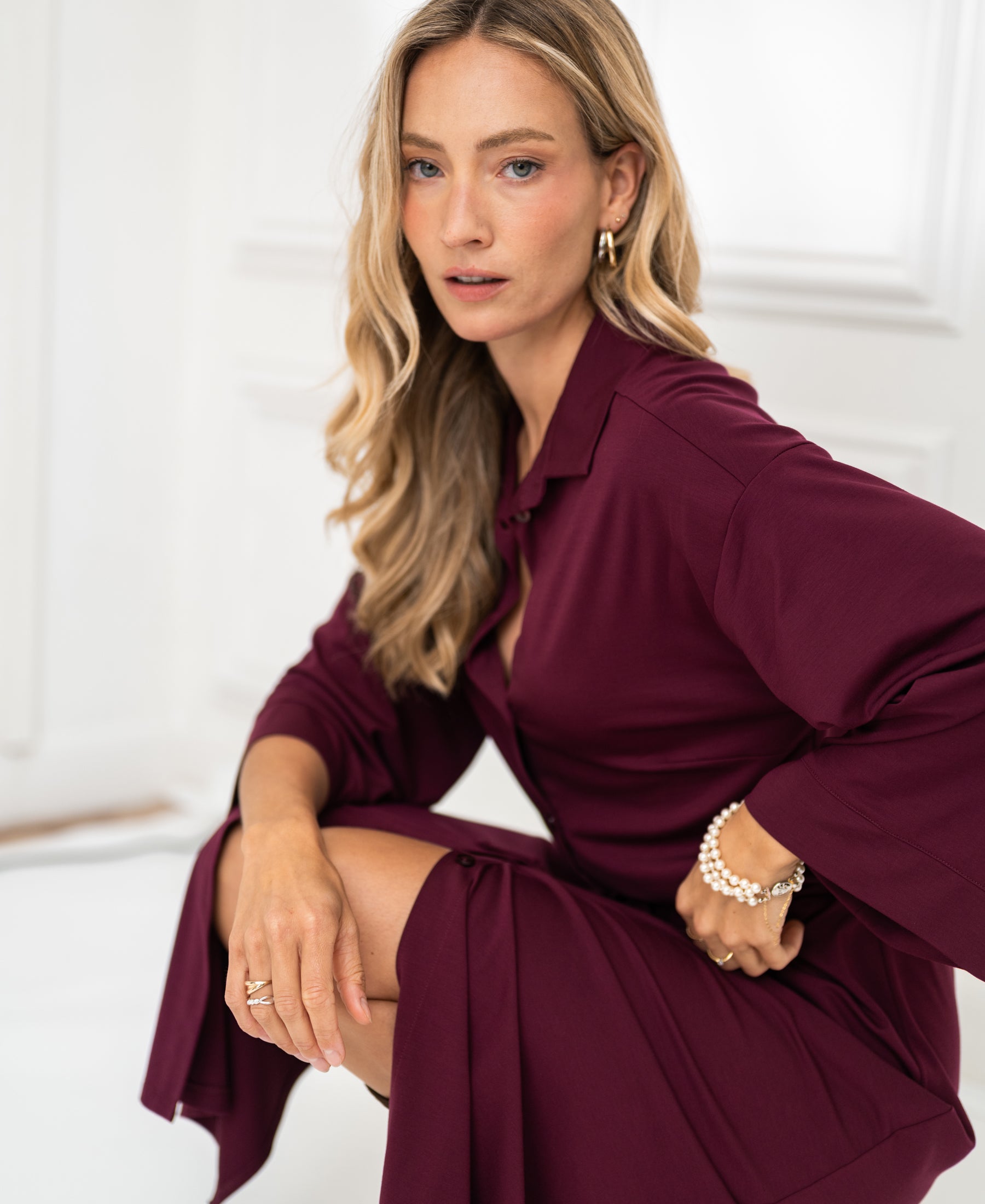 A woman poses indoors wearing a Bordeaux button-down dress by PLEIN PUBLIQUE.