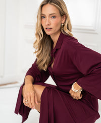 A woman poses indoors wearing a Bordeaux button-down dress by PLEIN PUBLIQUE.